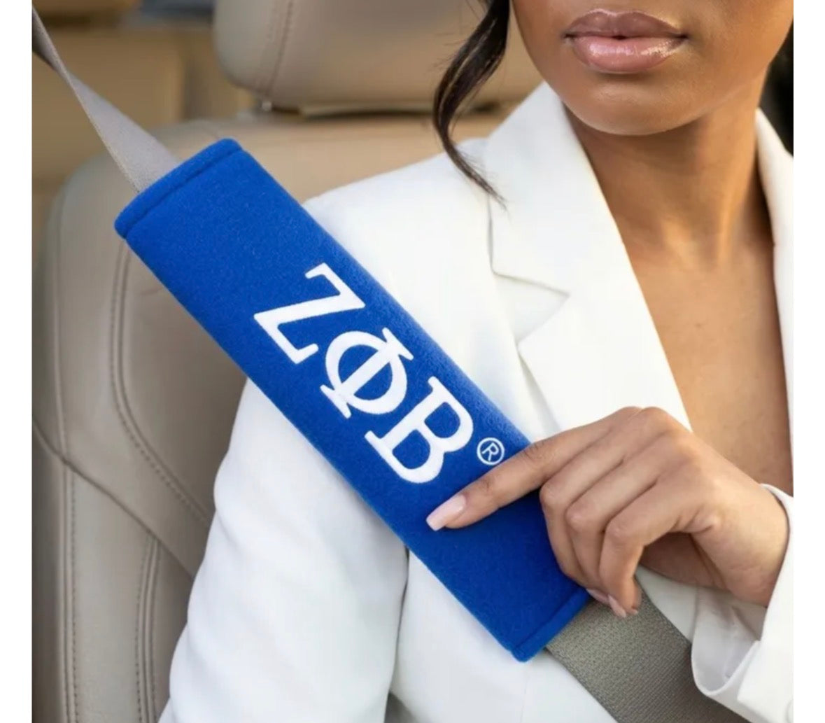 Soror in a white blazer holding a royal blue Zeta Phi Beta seat belt cover with white ZPB lettering across her shoulder belt.