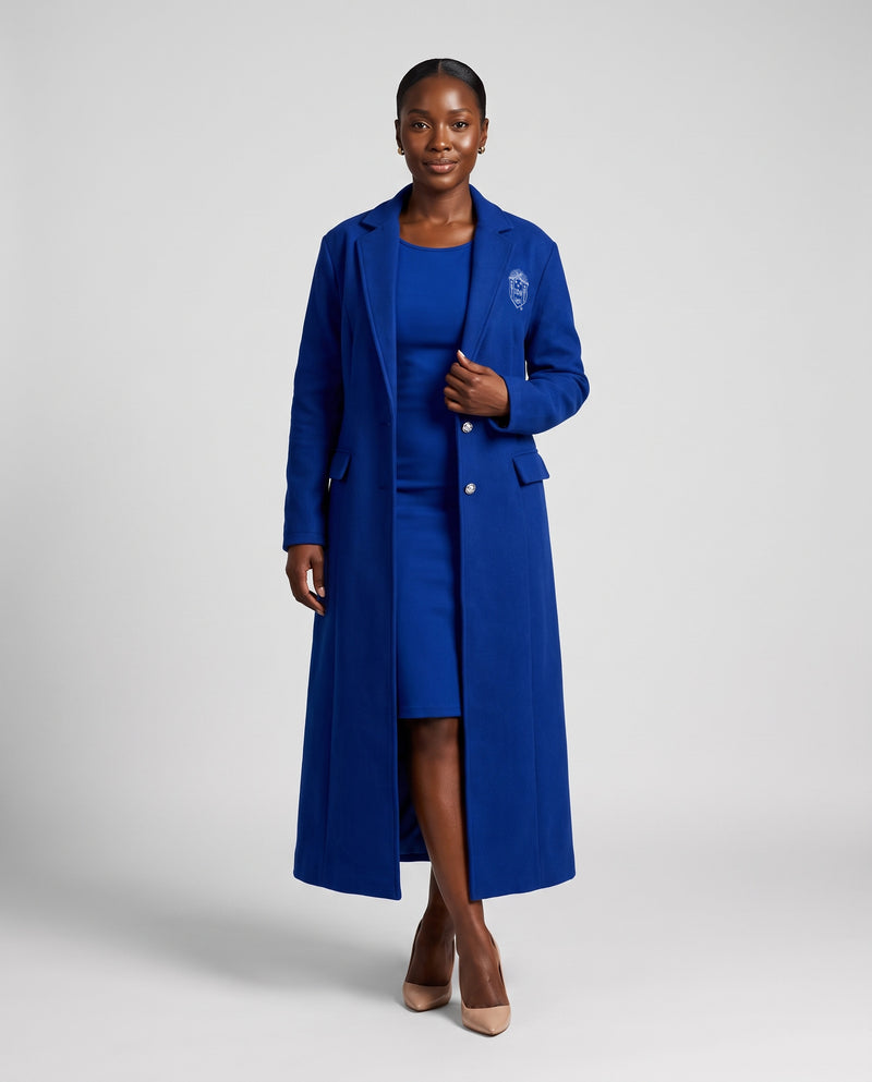 Woman wearing The Michelle: the ankle-length Royal Blue coat open over the matching sleeveless dress, Zeta Phi Beta shield on the chest