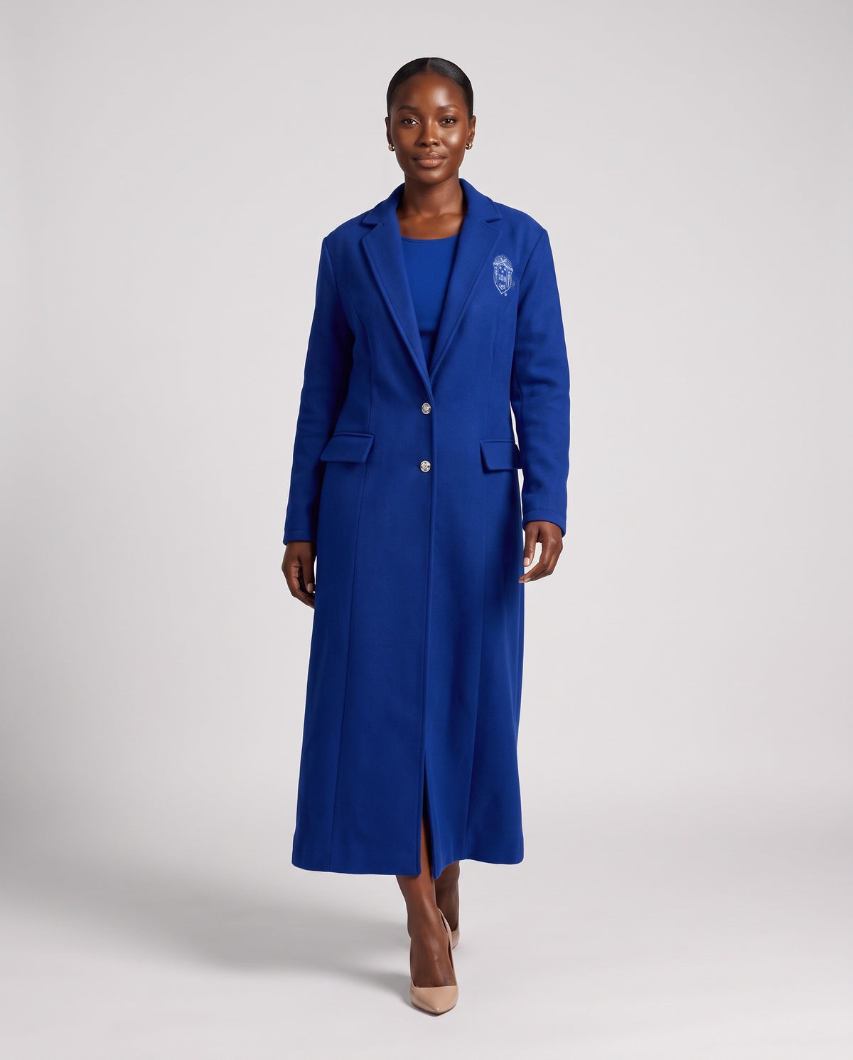 Woman walking in The Michelle ankle-length Royal Blue coat, buttoned, white Zeta Phi Beta shield over the chest