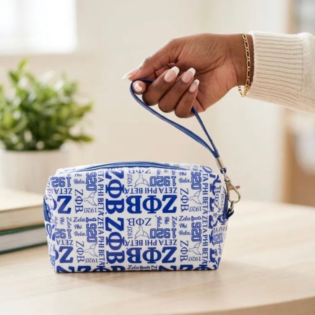 Zeta Phi Beta makeup bag in white with Royal Blue ZΦB, 1920 and dove print, held by its blue wristlet strap